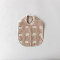 A Fuwara muslin bib made with cotton Japanese gauze in light brown, featuring a stitched pattern of white hedgehogs and matching striped trimming.