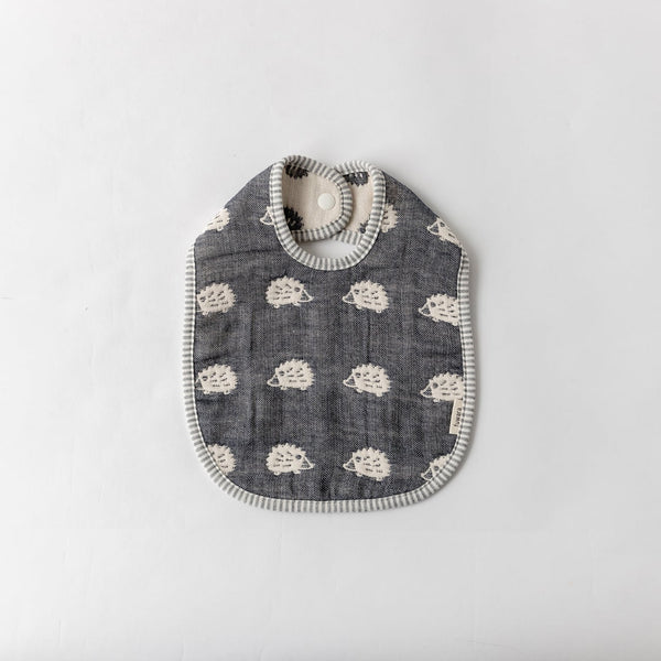 A Fuwara muslin bib made with cotton Japanese gauze in navy blue, featuring a stitched pattern of white hedgehogs and grey striped trimming.