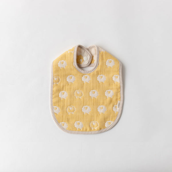 A Fuwara muslin bib made with cotton Japanese gauze in sunny yellow, featuring a stitched pattern of white sheep and matching striped trimming.