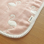 A closeup of the corner of a Fuwara, Japanese gauze baby muslin in pink, stitched with white flamingos. The edge of the cloth is trimmed in grey stripes.