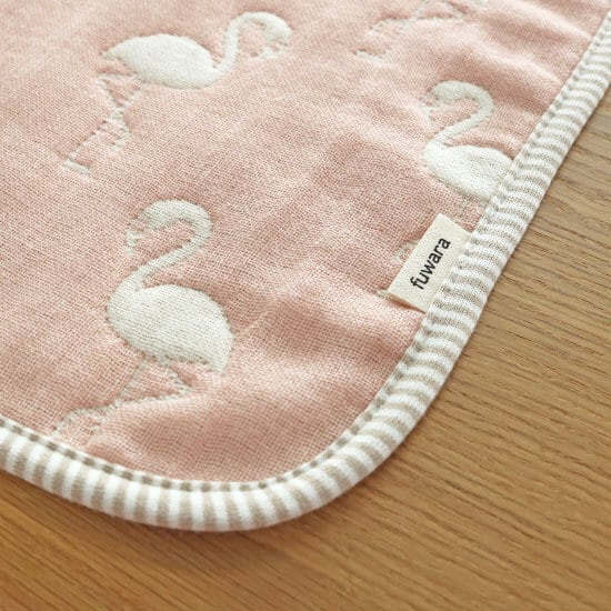 A closeup of the corner of a Fuwara, Japanese gauze baby muslin in pink, stitched with white flamingos. The edge of the cloth is trimmed in grey stripes.