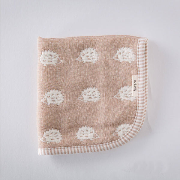 A closeup of a folded Furwara multipurpose small muslin in brown, made of Japanese cotton gauze. The fabric features a pattern of white, woven hedgehogs and a striped trim edge.