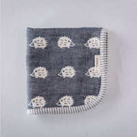 A closeup of a folded Furwara multipurpose small muslin in navy blue, made of Japanese cotton gauze. The fabric features a pattern of white, woven hedgehogs and a striped trim edge.