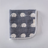 A closeup of a folded Furwara multipurpose small muslin in navy blue, made of Japanese cotton gauze. The fabric features a pattern of white, woven hedgehogs and a striped trim edge.