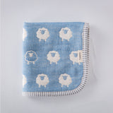 A closeup of a folded Furwara multipurpose small muslin in light blue, made of Japanese cotton gauze. The fabric features a pattern of white, woven sheep and a striped trim edge.