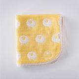 A closeup of a folded Furwara multipurpose small muslin in yellow, made of Japanese cotton gauze. The fabric features a pattern of white, woven sheep and a striped trim edge.