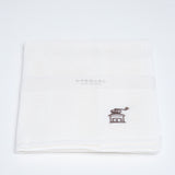 A folded white muslin cloth with a small brown coffee mill motif embroidered in the corner. Designed and made by Harada Orimono and available in NiMi Projects UK.