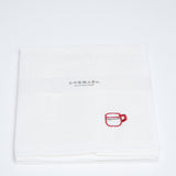 A folded white embroidered muslin cloth with a small red motif of a coffee mug in the corner. Designed and made by Harada Orimono and available in NiMi Projects UK.