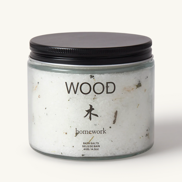Homework Wood aroma bath salts in a short cylindrical glass jar with black metal screwtop lid.