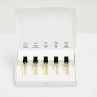 Set of five small bottles of perfume with labels in a white box on a light gray background