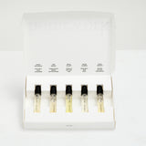 Set of five small bottles of perfume with labels in a white box on a light gray background