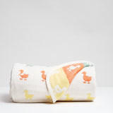 A Japanese cotton muslin gauze blanket with a pattern of rows of multicolour duck motifs with one side folded up to show it's reverse side. Made in Japan by Fuwara and available at NiMi Projects UK.