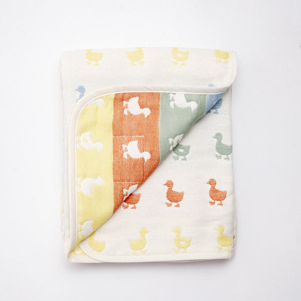 A folded, reversible off-white Japanese cotton muslin blanket with a pattern of rows of multicolour duck motifs. The corner is folded upward to show both sides of the fabric. Made Fuwara in Japan and on show at NiMi Projects UK.