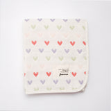 A folded Japanese off-white cotton muslin blanket patterned with rows of multicolour hearts. Available at NiMi Projects UK and made by Fuwara in Japan.	