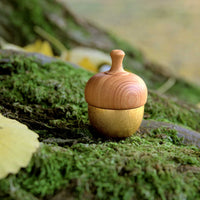 A Kuon Madoka acorn-shaped singing bowl chime, with a gold-coloured brass bell base and walnut wood cap displayed on a bed of green moss. The mallet is hidden inside. Designed by Yotsukawa Seisakusho for its Kisen brand.