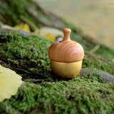 A Kuon Madoka acorn-shaped singing bowl chime, with a gold-coloured brass bell base and walnut wood cap displayed on a bed of green moss. The mallet is hidden inside. Designed by Yotsukawa Seisakusho for its Kisen brand.