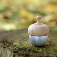 A Kuon Madoka acorn-shaped singing bowl chime, with a silver-coloured brass bell base and walnut wood cap displayed outside on a cut tree trunk. The mallet is hidden inside. Designed by Yotsukawa Seisakusho for its Kisen brand.