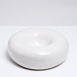 A side-view of a large, white and rotund donut-shaped serving dish, made by Maki Baxter and on display at NiMi Projects UK.