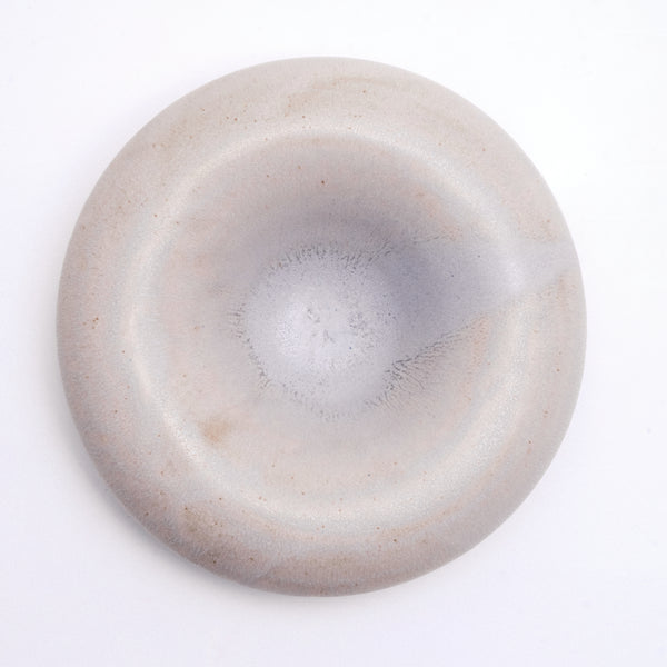A top view of a large, grey and rotund ceramic, donut-shaped serving dish, made by Maki Baxter and on display at NiMi Projects UK. The grey ceramic is lightly flecked for detail.