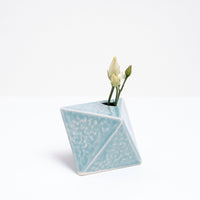 A diamond-shaped, Japanese porcelain bud vase in pale blue, holding a few sprigs of white flower buds. On show at NiMi  Projects UK.