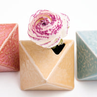 A diamond-shaped, yellow, Japanese porcelain bud vase holding a shite flower with pink-edged petals. Available at NiMi Projects UK.