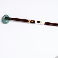 A green sora-mame bean-shaped Japanese, Mino-yaki hashioki chopstick rest, with a pair of dark brown lacquered chopsticks. Available at NiMi Projects UK.