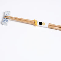 A white and blue speckled Japanese pillow-shaped, Mino-yaki hashioki chopstick rest, with a pair of bamboo chopsticks. On show at NiMi Projects UK.