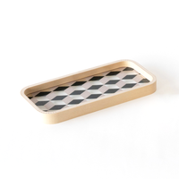 A rectangular Moheim GMT Pen Tray, with wood sides that curve at the corners and a transparent base featuring a geometric pattern of black and white tesselating diamonds.