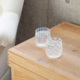 Two clear, Japanese glass cups with translucent white aburidashi geometric patterns — one vertical stripes, the other checked — display on a wooden surface. Made in Japan by Hirota Glass and designed by Moheim.