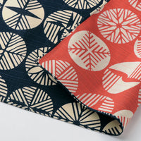 A detail of a Musubi furoshiki wrapping cloth featuring a pattern of circles filled with Japanese pine motifs in red on one side and blue on the other.