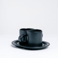 Ceramic Japan Pair Cups — two black porcelain semicircle half cups — sit facing each other on a specially designed shared saucer, on display at NiMi Projects UK