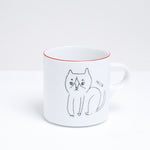  A white porcelain Ennui mug, designed by Angle Ceramics in Japan and available at NiMi  Projects, featuring an illustration of a cute cat and the words “Meow” and a red rim.
