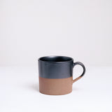 An earthenware mug half-dipped from the top in a graphite black glaze. Made in Japan by Angle ceramics and pictured at NiMi Projects UK.