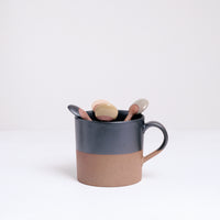 An earthenware Angle Soil mug half-dipped from the top in a graphite black glaze. Made in Japan by Angle ceramics and pictured at NiMi Projects UK with a selection of different coloured Angle ceramic spoons that are also dipped in similar glazes.