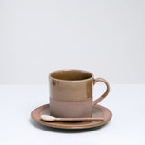 An earthenware Angle Soil mug, made in Japan and dipped in a glossy taupe glaze. Pictured at NiMi Projects UK with a matching earthenware spoon, both placed on top of a matching Angle Soil saucer.