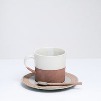 An earthenware Angle Soil mug, made in Japan and dipped in a silky white glaze. Pictured at NiMi Projects UK with a matching earthenware spoon, both placed on top of a matching Angle Soil saucer.