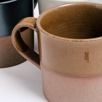 Closeup detail of an Angle ceramic Soil mug’s side and handle, showing its upper half of glossy taupe glaze and lower half of exposed orange earthenware clay. Available at NiMi Projects UK.