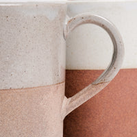 Closeup detail of an Angle ceramic Soil mug’s side and handle, showing its upper half of glossy grey glaze and lower half of exposed orange earthenware clay. Available at NiMi Projects UK.