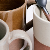 Closeup detail of several Angle ceramic Soil mugs showcasing their dipped glazes in taupe, grey and white and their lower halvesof exposed orange earthenware clay. Available at NiMi Projects UK.