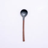 A mino-yaki earthenware tea spoon made in Japan by Angle and available at NiMi Projects UK. Its handle is left as exposed orange clay, while its head has been dipped in a graphite black glaze.