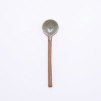 A mino-yaki earthenware tea spoon made in Japan by Angle and available at NiMi Projects UK. Its handle is left as exposed orange clay, while its head has been dipped in a glossy grey glaze.