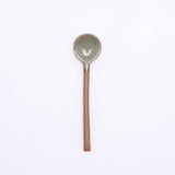 A mino-yaki earthenware tea spoon made in Japan by Angle and available at NiMi Projects UK. Its handle is left as exposed orange clay, while its head has been dipped in a glossy grey glaze.