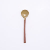 A mino-yaki earthenware tea spoon made in Japan by Angle and available at NiMi Projects UK. Its handle is left as exposed orange clay, while its head has been dipped in a glossy yello glaze.