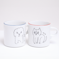 A pair of white Ennui porcelain mugs, made by Angle Ceramic in Japan and on show at NiMi Projects UK. On the left the mug features an illustration of a fluffy puppy and the words "Bow wow," on the right the mug features a cat and the word "Meow"