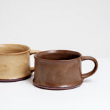 Two low and wide, flat ceramic mugs; one with a rich brown glaze and the other in a beige yellow. Made in Japan by Angle and available at NiMi Projects UK.