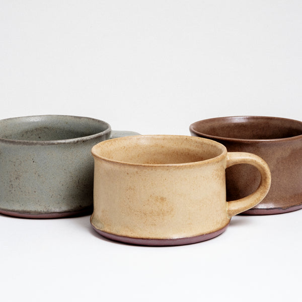 Three low and wide, flat Japanese ceramic mugs, each a different colour — green gray, beige yellow and rich brown. Made by Angle and on show at NiMi Projects UK.