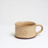 An extra wide, low, flat-based mug with a satin glaze in mottled beige yellow, made by Angle in Japan and on show at NiMi Projects UK.