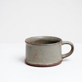 A hand-made, wide and low mug with a flat base and a satin glaze in mottled grey green, made by Angle in Japan and on show at NiMi Projects UK.
