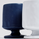 Closeup of a blue and a white, satin-glazed stemmed (or footed) mug with a round base. Hand made in Japan by Angle and available at NiMi Projects UK.

