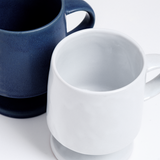 Closeup of the tops of blue and white, satin-glazed stemmed (or footed) mugs with a round bases and curved handles. Hand made in Japan by Angle and available at NiMi Projects UK.
